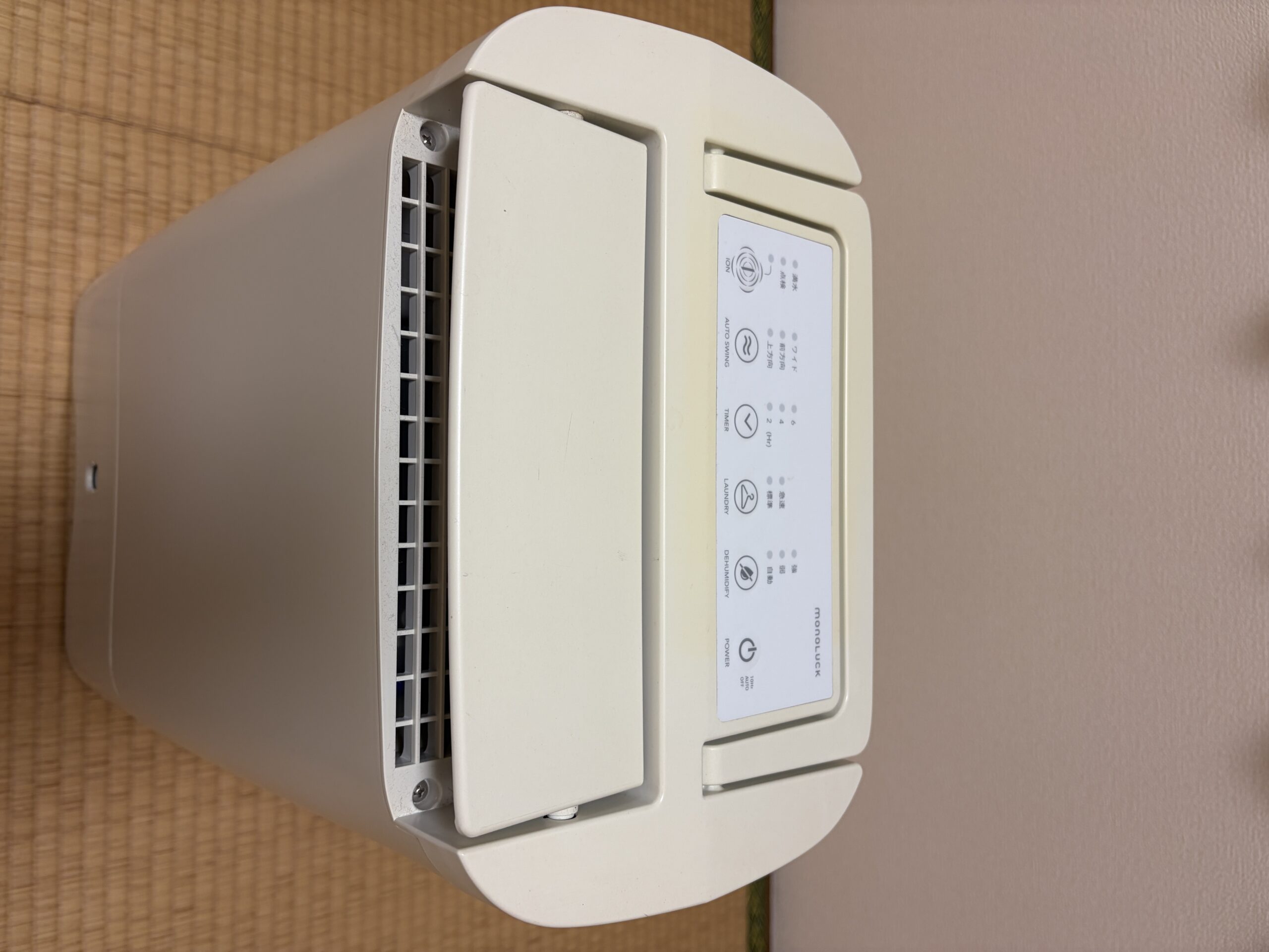 製品写真: monoLUCK DDA10 本体上部の操作パネル（monoLUCKロゴ・POWER/LAUNDRY/DEHUMIDIFY ボタンが視認できる角度・畳の上設置）